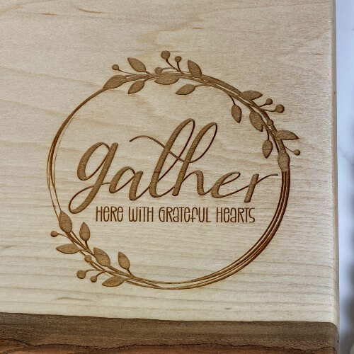 Live edge charcuterie board with "gather here with grateful hearts," engraved in the corner.