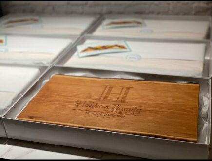Engraved live edge charcuterie board shown in packaging for a wholesale order.