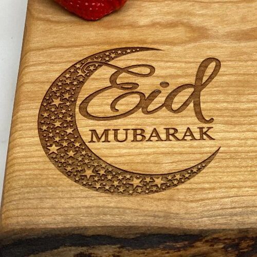 Close up of Eid Mubarak engraved in the corner of a live edge charcuterie board.